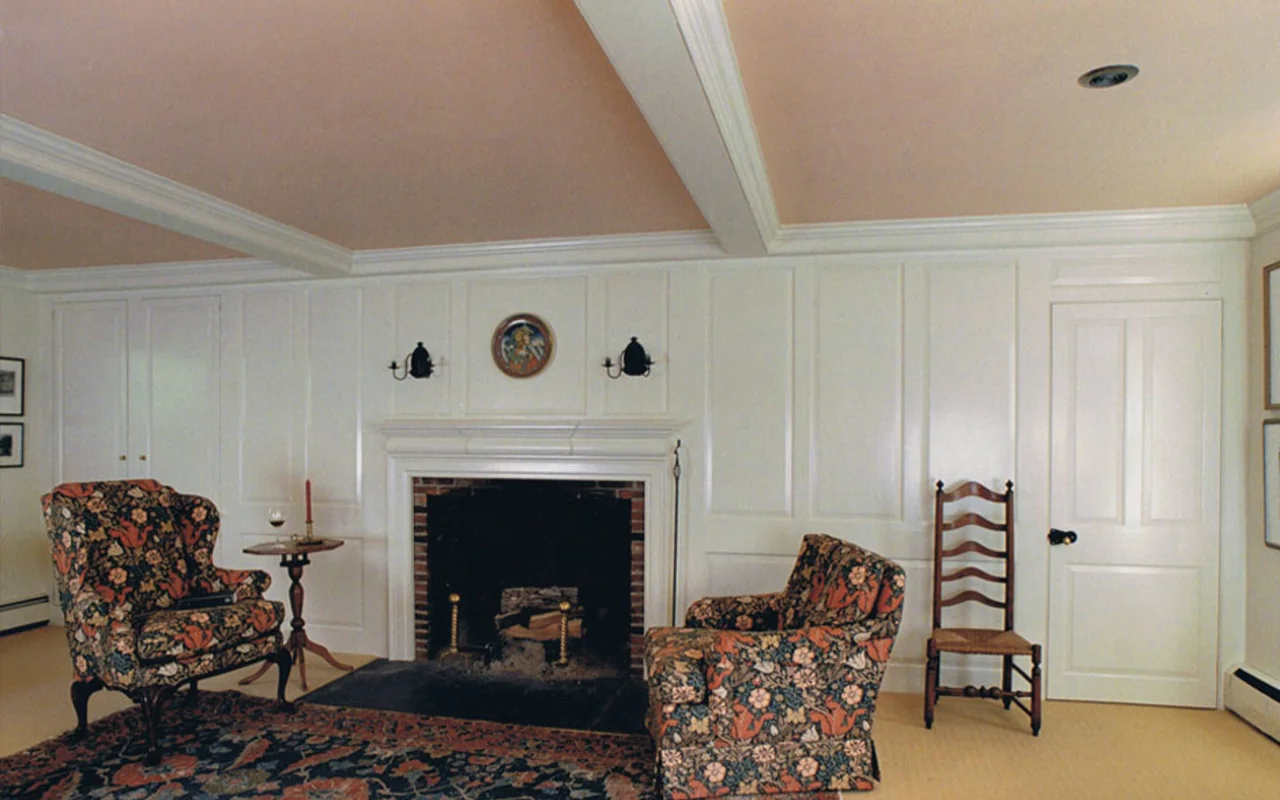 A finished colonial living room with white raised-panel walls, a fireplace with marble surround, and crown molding, built by Britten Woodworking